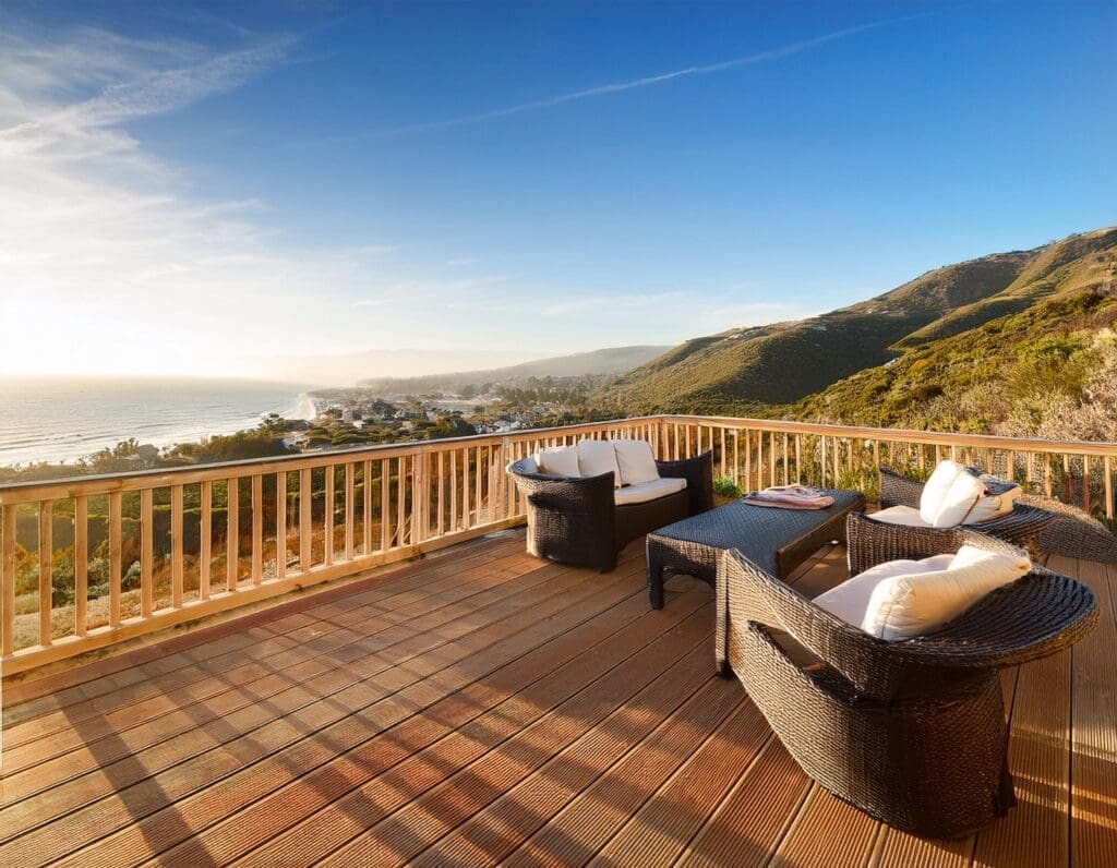 A spacious wooden deck furnished with outdoor seating, overlooking a coastal California landscape. J Kidd Construction
